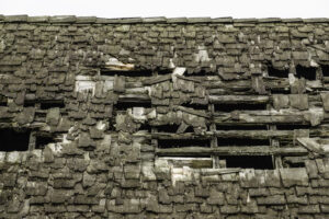 Ravages of time and neglect: Detail of shingled roof of old wood-frame building with gaping holes and many exposed nails, for themes of upkeep and a lack thereof