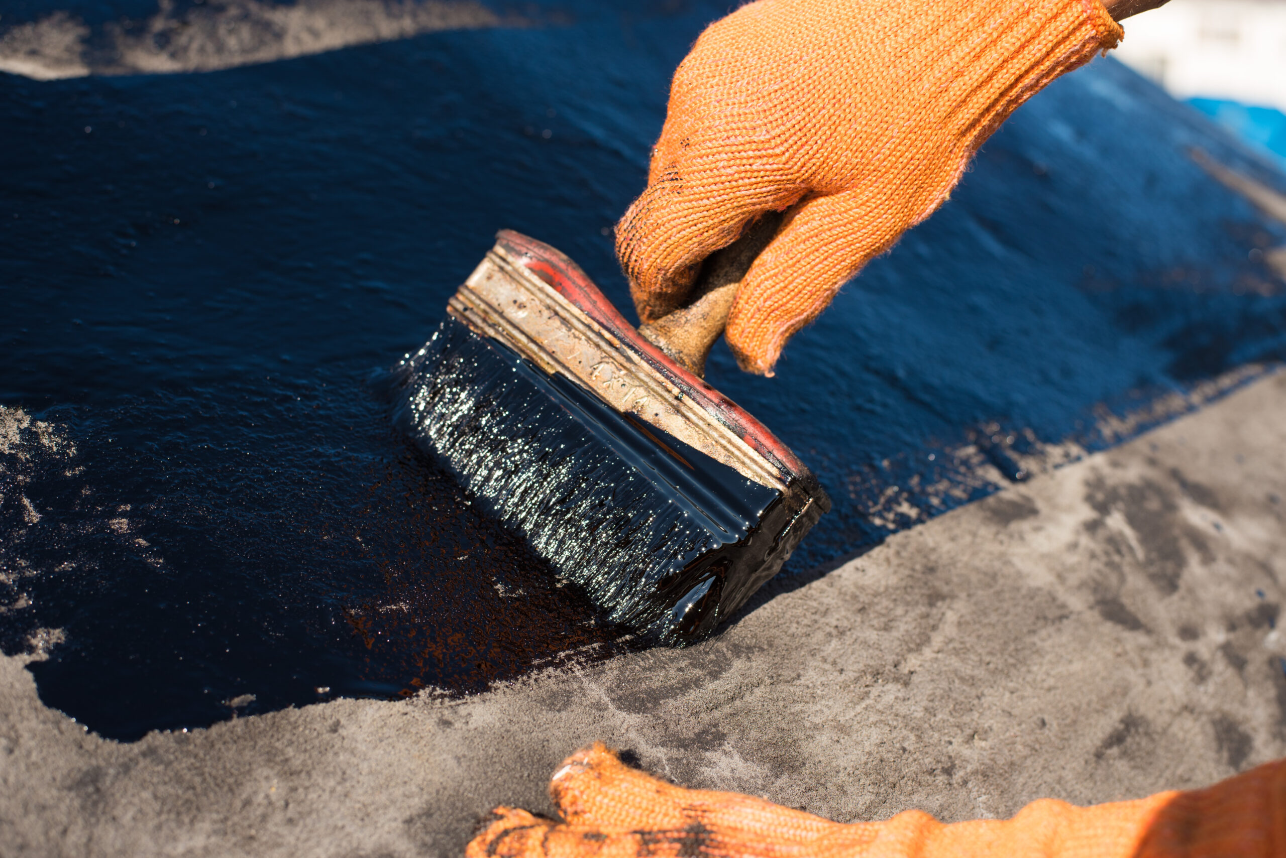 A worker brushes liquid over a roof surface